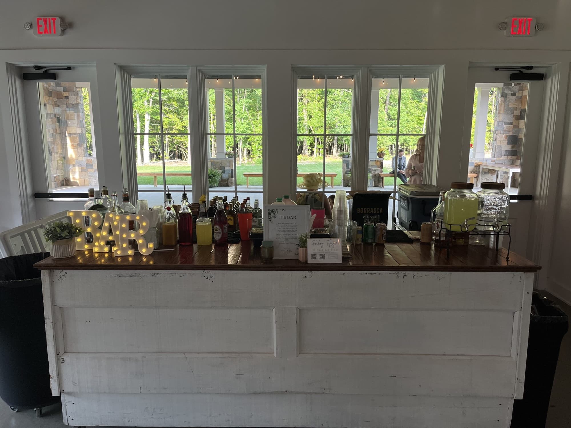 The Pop Up Bar with lit BAR letters, drink dispensers and bottles in a bright venue hall with tall windows.