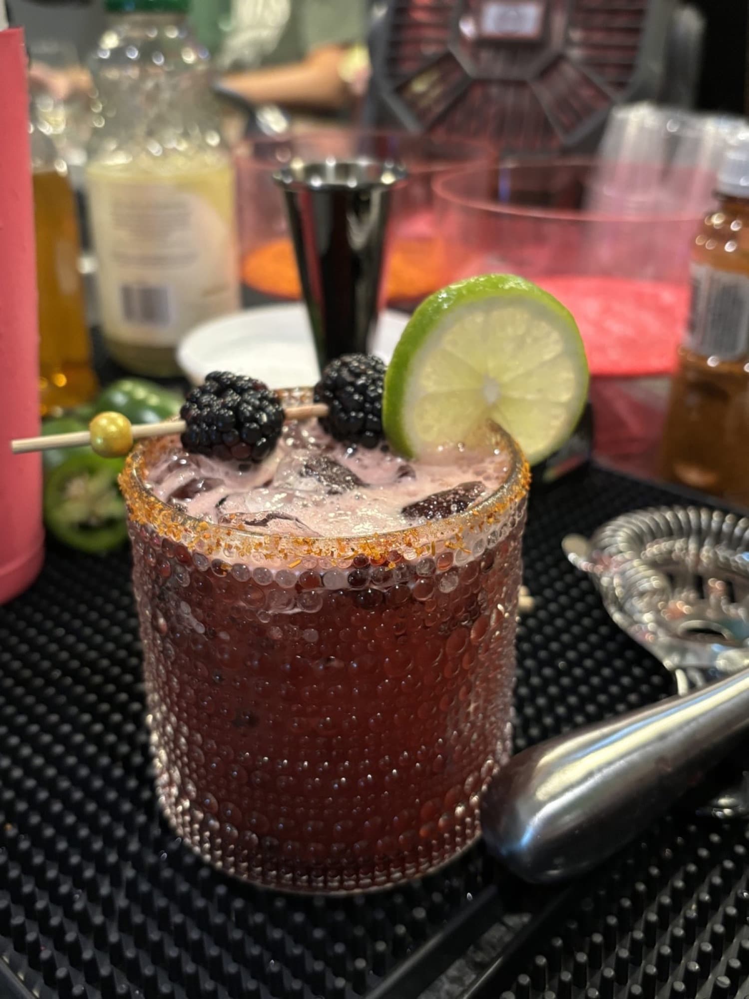 A blackberry cocktail with a chili-salt rim and a lime wheel on the bar mat.