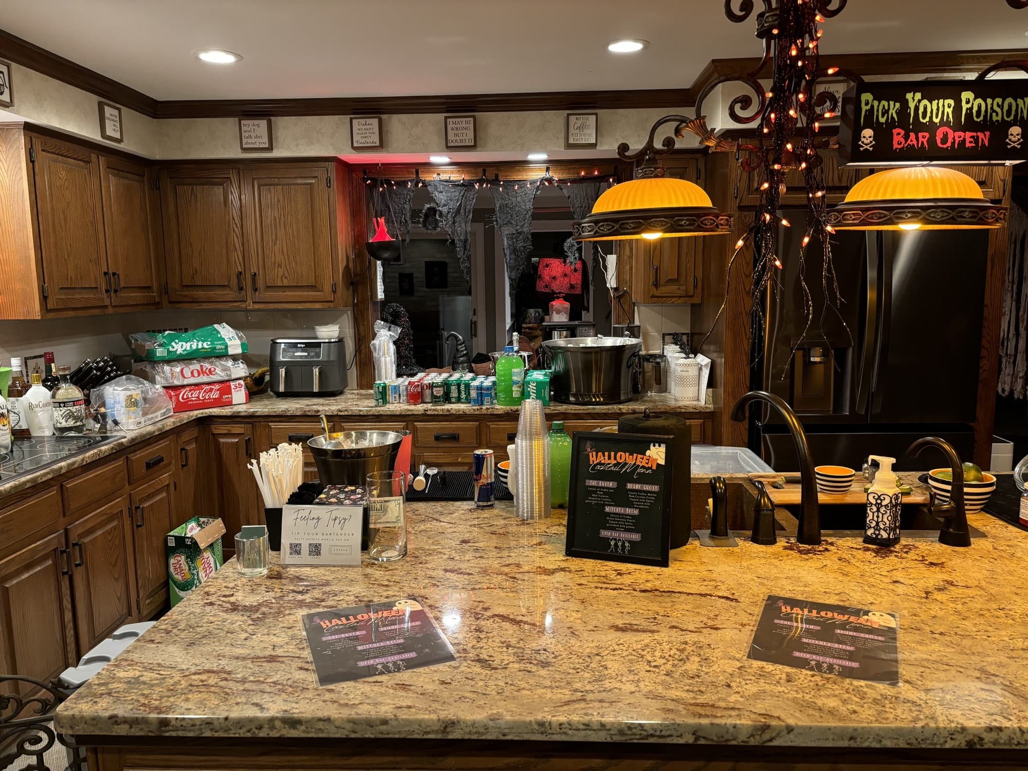 A Halloween party bar on a kitchen island with themed drink menus and a Pick Your Poison sign.