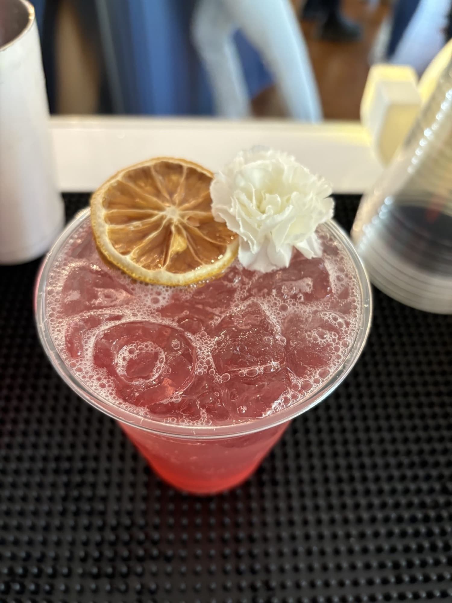 A pink signature cocktail finished with a dried orange wheel and a white carnation.
