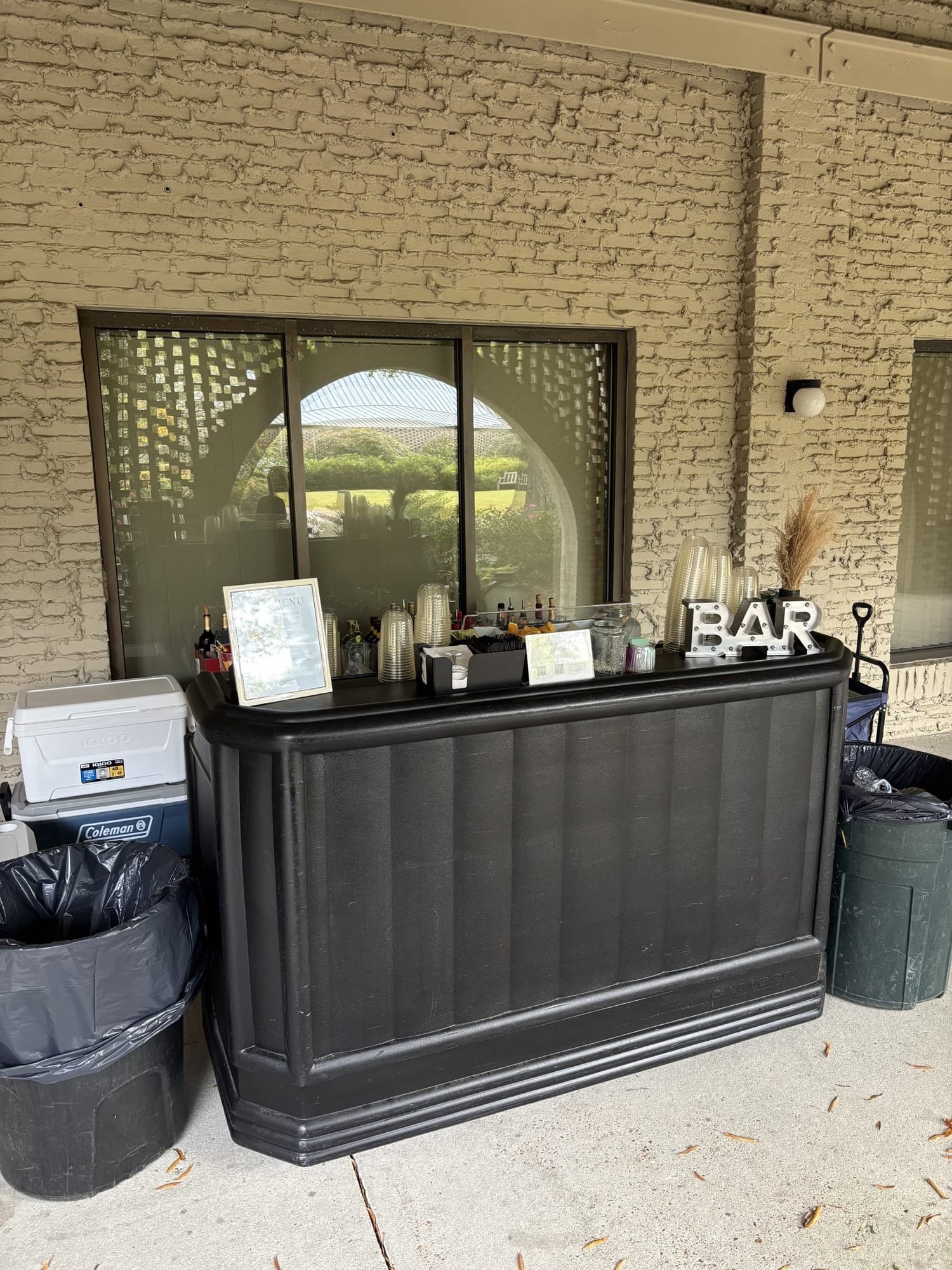 The Pop Up Bar in black, with its coolers and trash cans in place, on a covered brick patio at a venue.