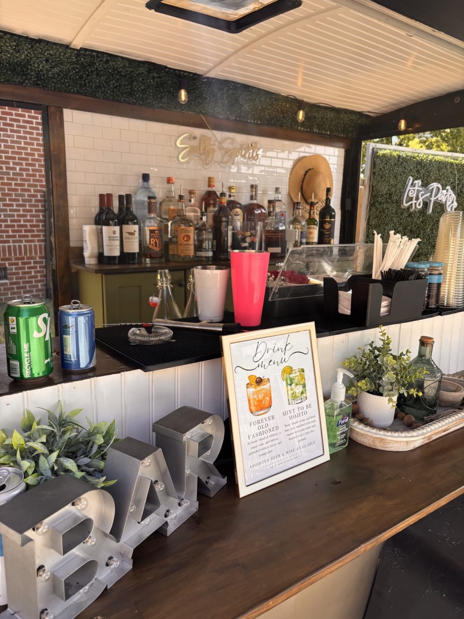 Inside The Blair: the back bar, the Salty Spirits neon, the greenery wall and a framed drink menu.